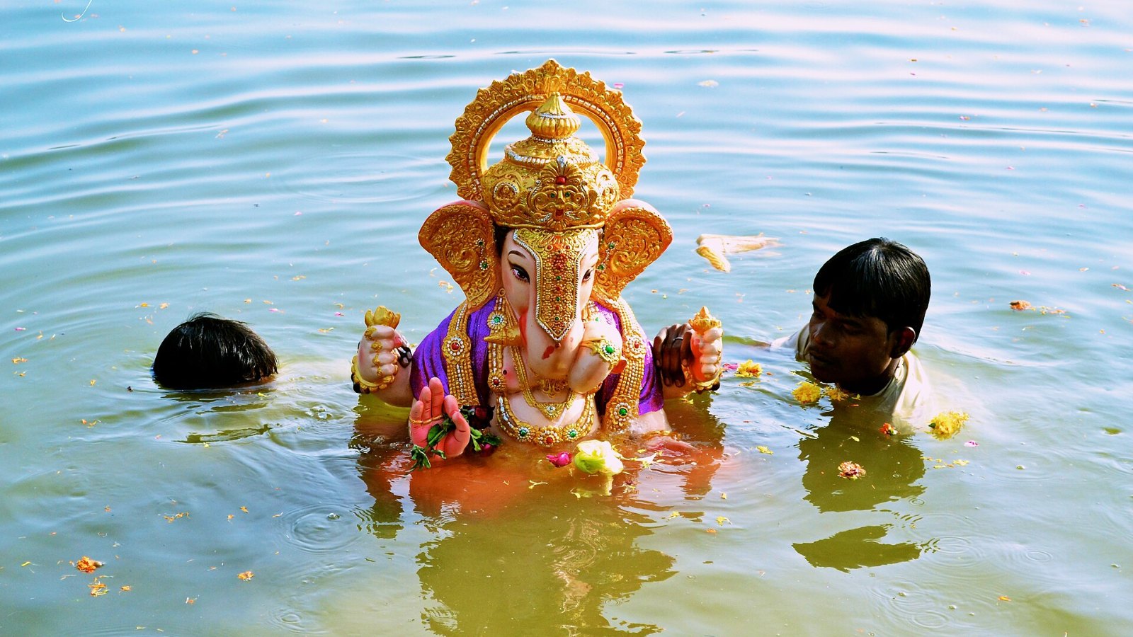A clay Ganesha idol being immersed in water during visarjan