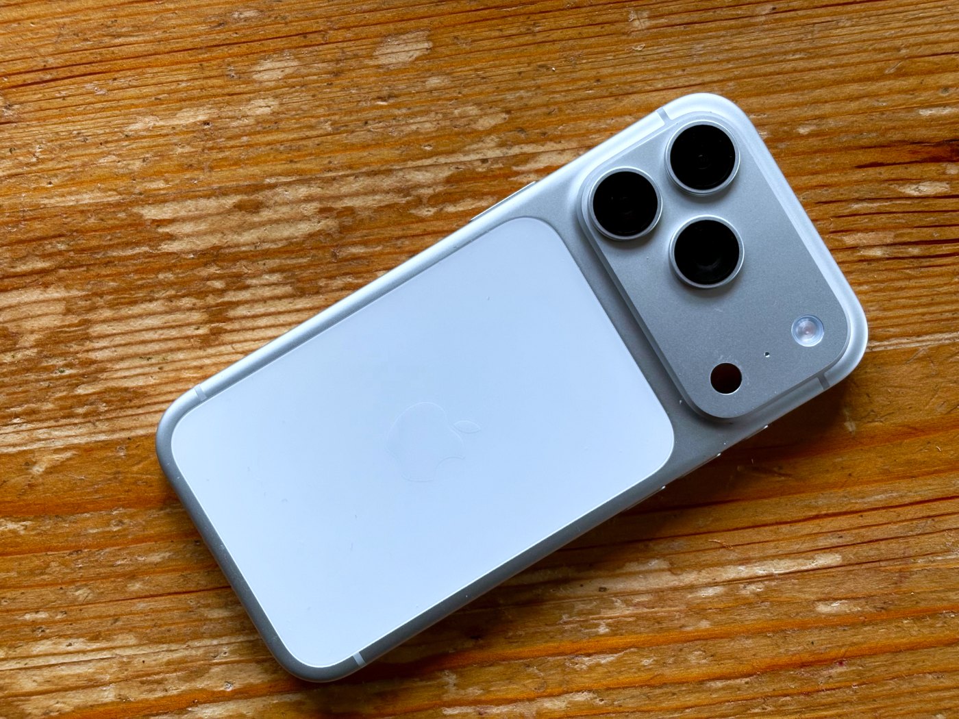 A silver iPhone 17 Pro lying on a wooden table, showing its triple camera
